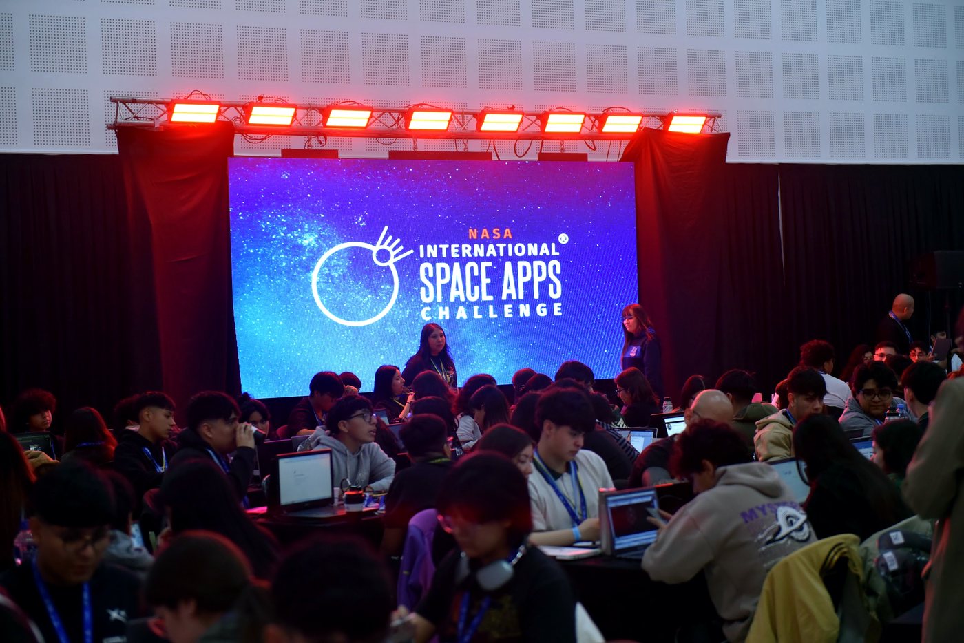 La sala completa durante la apertura, con el escenario y la pantalla de Space Apps